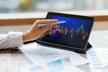 Focused on strategy, an investor holds a market analysis report, assessing stock performance with a tablet displaying real-time fluctuating graphs beside them.