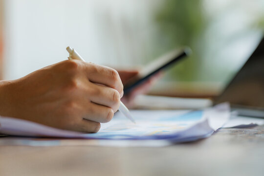 Captured in the image is a hand gripping a pen, directing attention to a sheet summarizing the monthly KPI performance review.