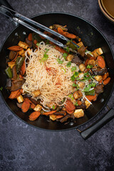 Vegan Stir fried eggplant, carrot and pepper served with rice noodles in cast iron wok