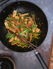 Vegan tofu, beans andcarrot stir fry in black wok, chopsticks