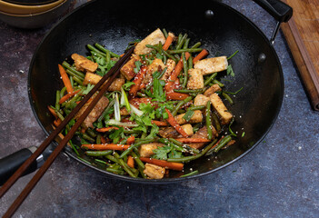 Vegan tofu, beans andcarrot stir fry in black wok, chopsticks