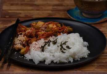 Vegan Korean tofu and kimchi, rice on black plate on bamboo mat