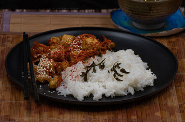Vegan Korean tofu and kimchi, rice on black plate on bamboo mat