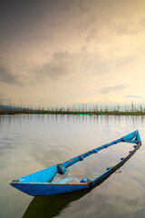Obraz premium Old blue wooden boat half-submerged in calm lake water under dramatic sunset sky