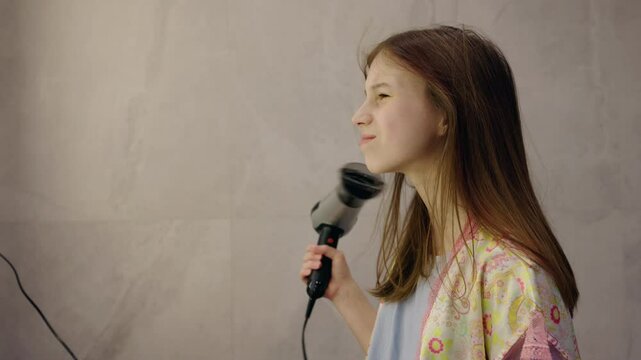 Teenage girl drying her hair with a blow dryer, smiling and enjoying a relaxing morning routine in a bright modern bathroom.