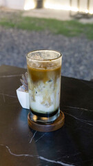 A refreshing iced coffee with milk served in a tall clear glass, showing beautiful swirling layers of coffee and cream