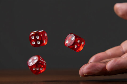 A hand rolling three red dice with red dots on a dark surface, symbolizing luck, chance, and gaming dynamics.