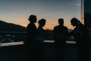 Silhouetted business people are seen shaking hands on a rooftop at sunset, symbolizing connection and partnership. The setting sun adds a dramatic and inspirational backdrop to the corporate