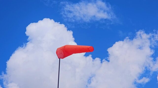  the orange windsock on a pole in strong wind against a blue sky and cloud , Airbag, wind direction, know which way the wind is blowing