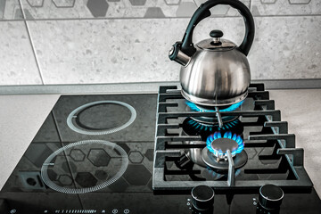 Blue fire from domestic kitchen stove top. Gas cooker with burning flames of propane gas. Silver pot kettle. induction stove