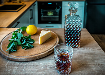 Glass of Alcohol Whiskey or Bourbon, Cheese, Lemon and mint on the kitchen table