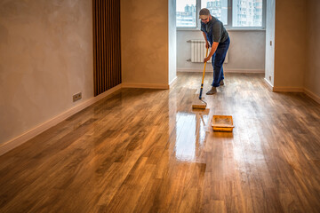 Parquet floor renovation. Lacquering wood floors. Worker carpenter uses a roller to coating floors.