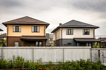 Two abandoned houses behind the fence with tiled roof under stormy cloud