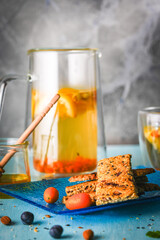 Crackers with flax seeds, nuts and sesame seeds on a blue plate and tea with lemon and honey on the table on a gray background.