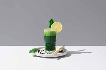 Jugo de espinacas adornado con una rodaja de limón y hoja de espinaca sobre una mesa blanca y...