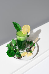 Jugo de espinacas adornado con una rodaja de limón y hoja de espinaca sobre una mesa blanca y fondo gris