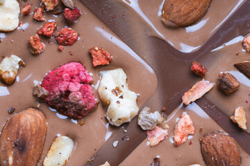 The process of making homemade chocolate. Nuts, freeze-dried raspberries and strawberries are laid out on liquid chocolate.