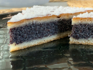 Two slices of poppy seed yeast cake sprinkled with powdered sugar, served on a black plate.