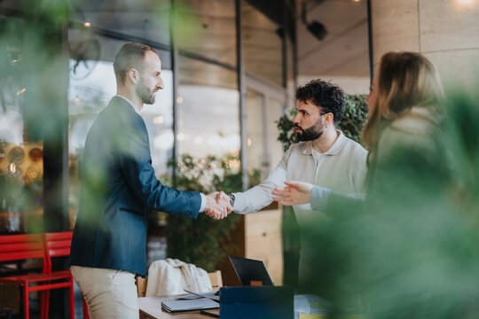Businesspeople shake hands across a table, symbolizing agreement and collaboration in a stylish and contemporary setting. A third person observes the interaction, portraying teamwork and communication - Powered by Adobe