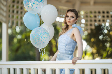 Young woman poses with blue balloons at a garden event during daylight hours in a serene outdoor...