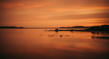 Fototapeta premium Serene orange sunset over tranquil waters with silhouette of shoreline and rock formations creates a peaceful and calming atmosphere