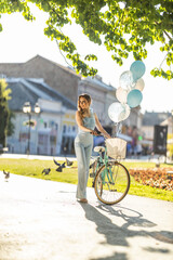 Young woman enjoying a sunny day outdoors with a bicycle and balloons in a colorful park