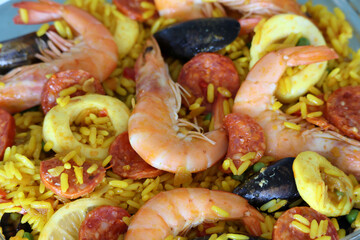 Delicious seafood paella with vibrant ingredients:  shrimps , calamari, chorizo, mussels, lemon and yellow rice closeup.