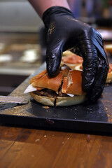 chef cogiendo una hamburguesa con sus manos con guantes y un cuchillo para servirla