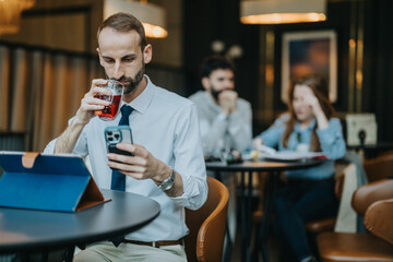 A man in professional attire looks at his smart phone and drinks at a cafe. The atmosphere is conducive to casual discussions and work, with other individuals visible in the background.