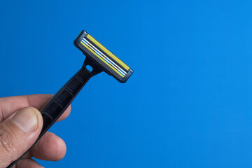 Hand Holding a Razor Against a Bright Blue Background for Grooming Needs