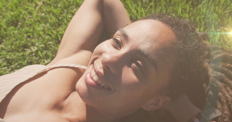 Image of light spots over smiling biracial woman lying in park