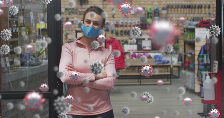 Obraz premium woman wearing blue mask, leaning against glass door inside sports shop, with sanitizer dispenser