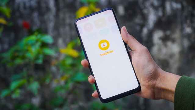 INDIA, DELHI - JANUARY 25, 2025: Hand Holding Smartphone Displaying Snaptube App Outdoors in a Green Environment