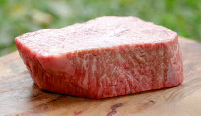 Close-up of a premium A5 Wagyu beef cut showing intense marbling, placed on a wooden board with a natural outdoor background.