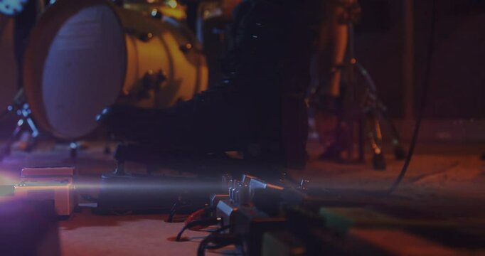 Guitar effects pedals glowing on stage floor among cables and blurred drum hardware in 3D render
