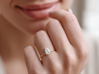 a blond woman's elegant hand with a breathtaking pear-cut diamond engagement ring on a gold band