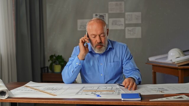 An architect sits in an office at a desk with blueprints