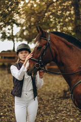 A young female equestrian stands near her horse and prepares for a competition.