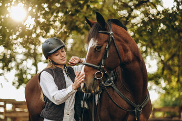 A young female equestrian stands near her horse and prepares for a competition.