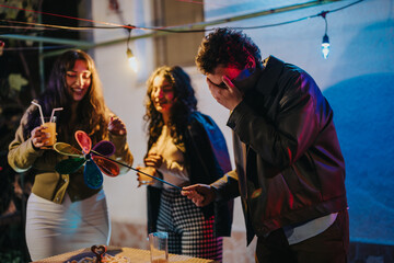 Group of friends enjoying a casual outdoor evening celebration filled with laughter, drinks, and cheerful moments. Decorative lighting and festive props enhance the lively atmosphere.