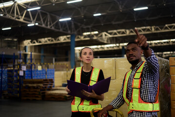 Caucasian female warehouse inspector and American-African warehouse worker are checking stock in warehouse to ensure quality and order before shipping to customer. Quality Assurance Logistics Business