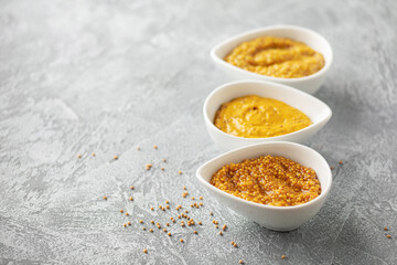 Mustard sauce in a bowl and seeds on a grey background.
