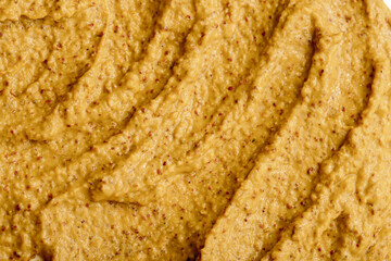 Mustard sauce with grains close-up. Hot spices as a background. Texture of Dijon mustard.