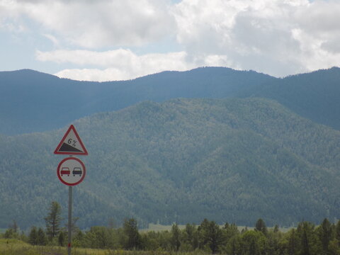 Altai Mountains - Road signs indicating reduced speed limits for drivers near mountainous terrain and lush green landscape during a cloudy day - Powered by Adobe