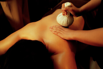 Hot herbal ball spa massage body treatment, masseur gently compresses herb bag on man body....