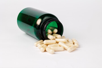 Spilled capsules from green bottle on white background, Close-up of beige capsules spilling out of a green plastic bottle onto a clean white background, representing supplements and healthcare.  