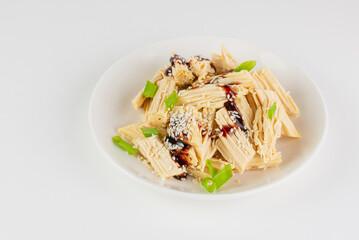 Tofu skin or yuba with green onions, sauce and sesame seeds in a white plate.  Asian dish isolated on white background