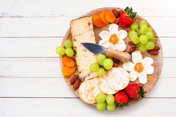 Summer theme charcuterie board against a white wood background. Variety of fruits, cheeses and crackers. Overhead view.