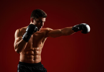 Man in boxing gear punching with glove, focused expression. Gym background with punching bag and workout equipment.