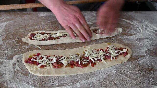 The cook seals the edges of the dough to bake pita bread with meat and cheese. 